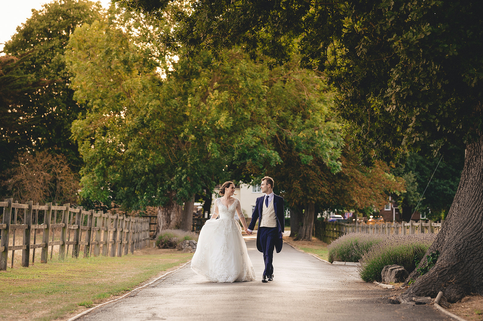 A newly married couple walking hand in hand beneath sunlit trees